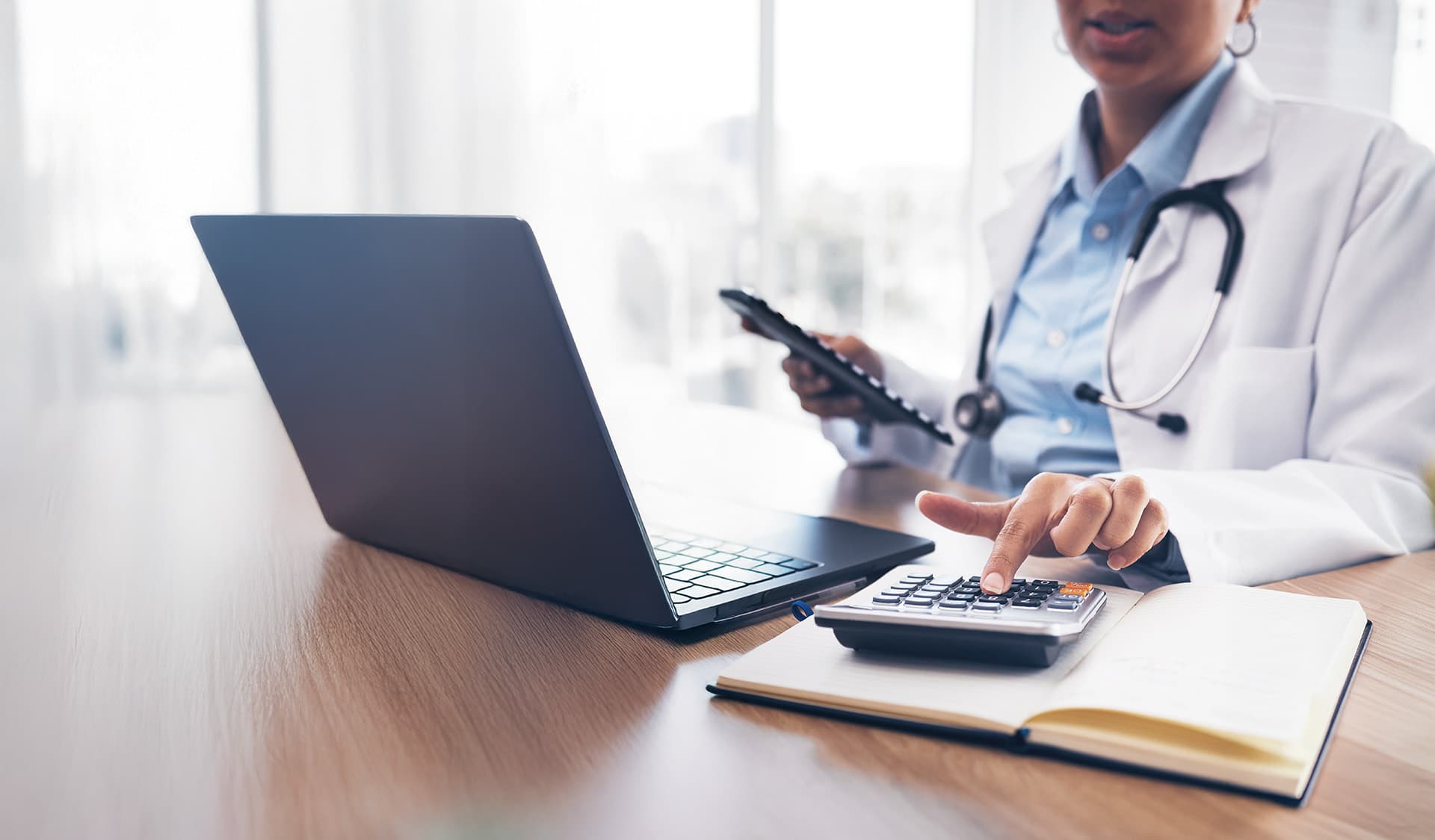 Phamacist sat at a laptop and using a calculator on the desk