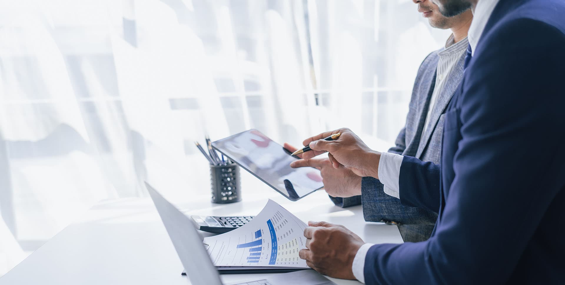 2 businessmen looking at performance on paper and a tablet