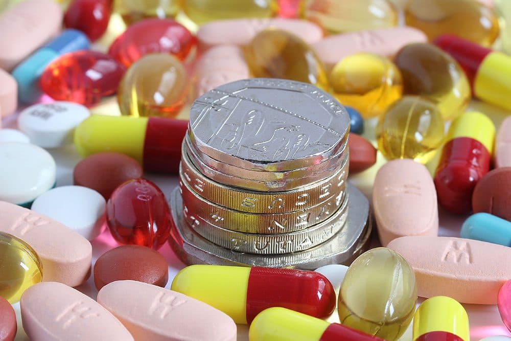 GBP coins stacked in the middle of medicine tablets and capsules