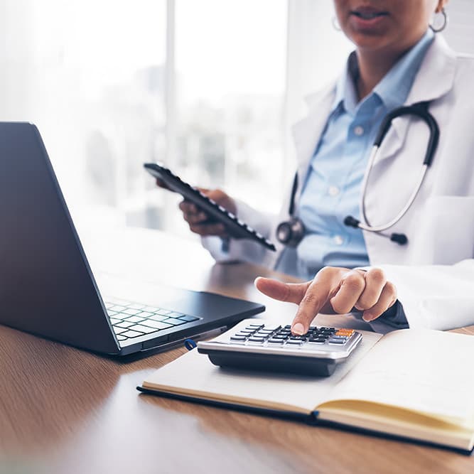 Phamacist sat at a laptop and using a calculator on the desk