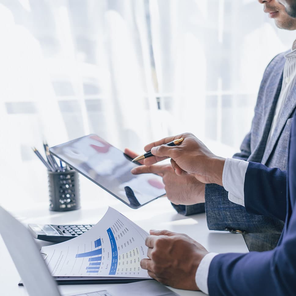 2 businessmen looking at performance on paper and a tablet